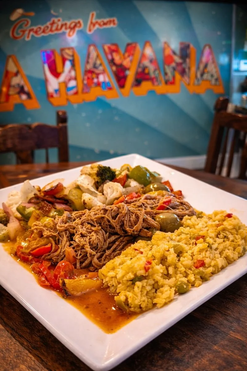 Plate of pulled pork, mashed potatoes with red peppers, and mixed vegetables on a wooden table with a colorful Hawaii sign in the background.