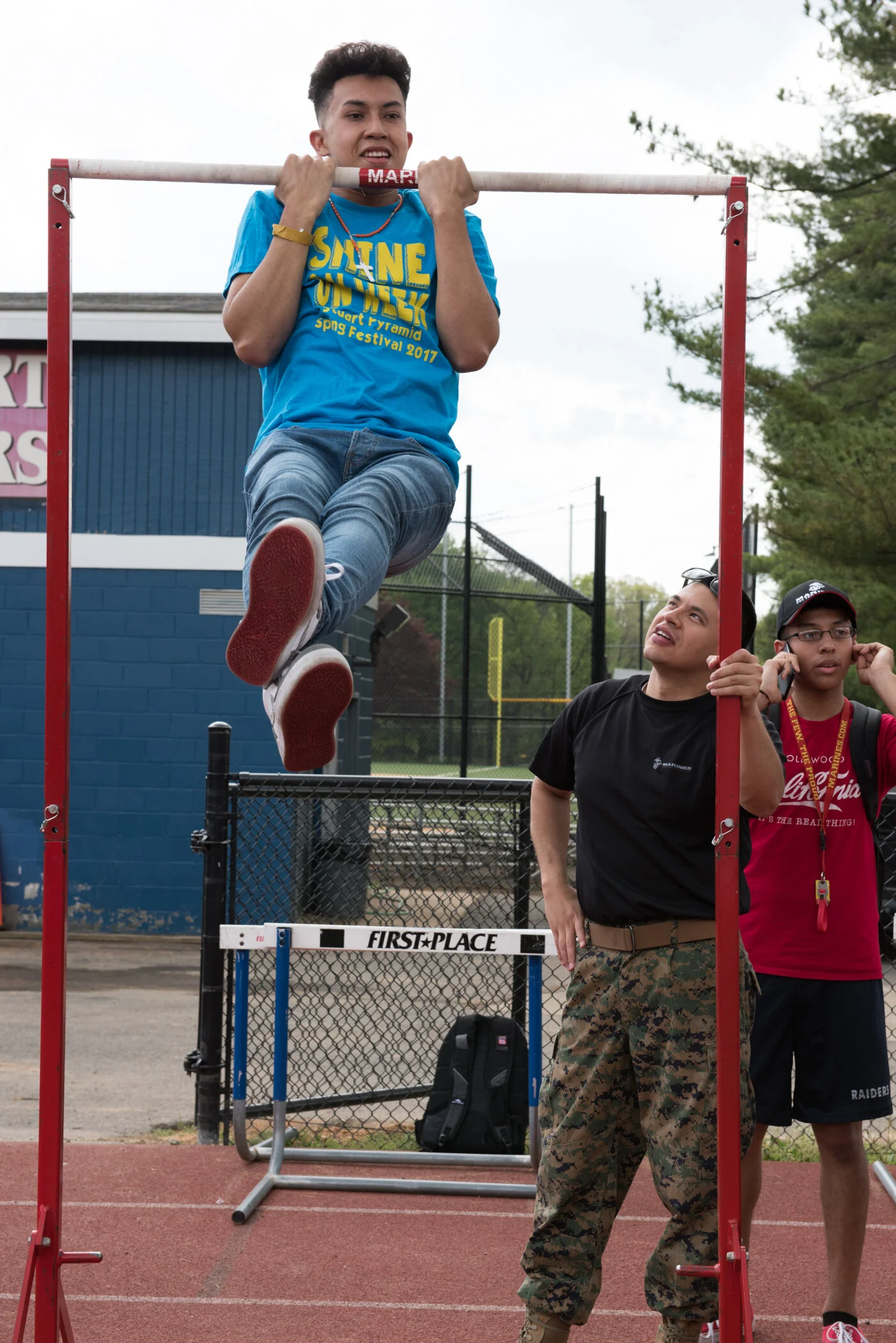 A young man doing a pole vault over a bar at an outdoor track and field event while two others watch.