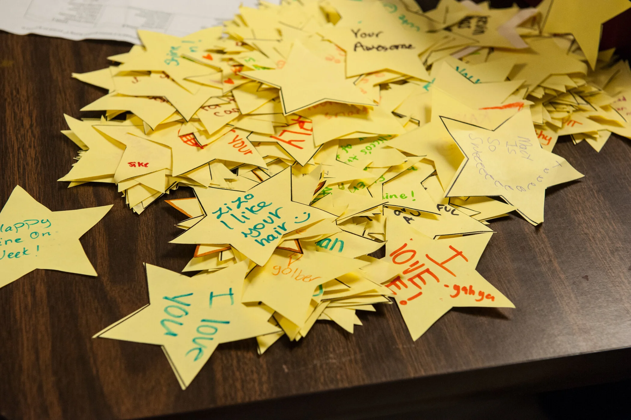 A pile of yellow star-shaped notes with handwritten messages and doodles on a wooden table.
