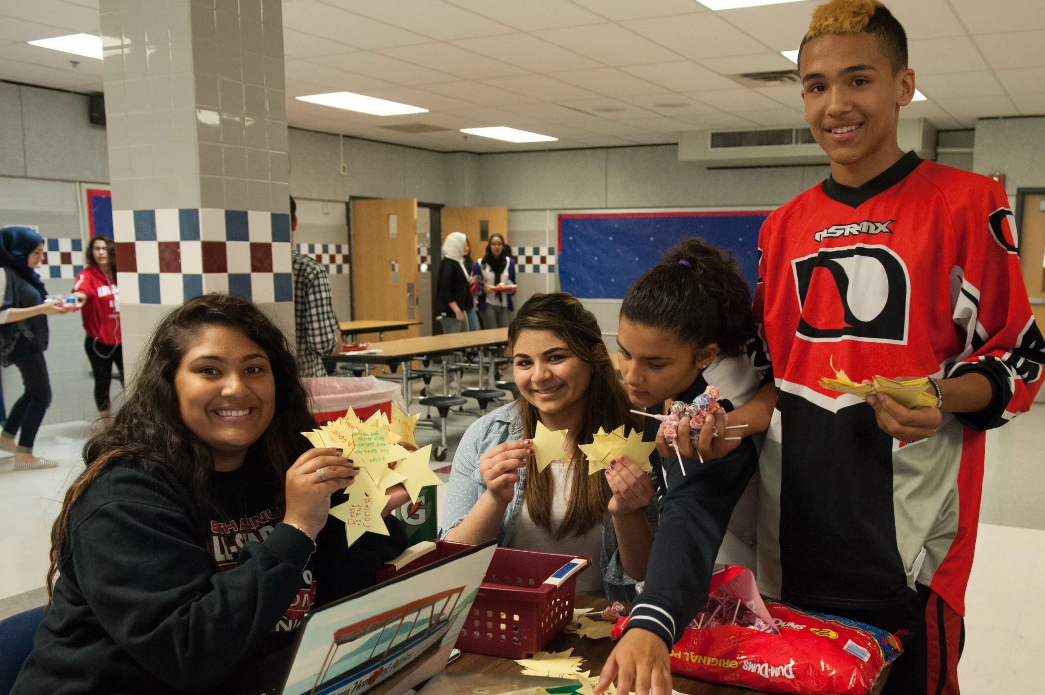 Group of students at a school cafeteria making and holding star-shaped paper crafts.