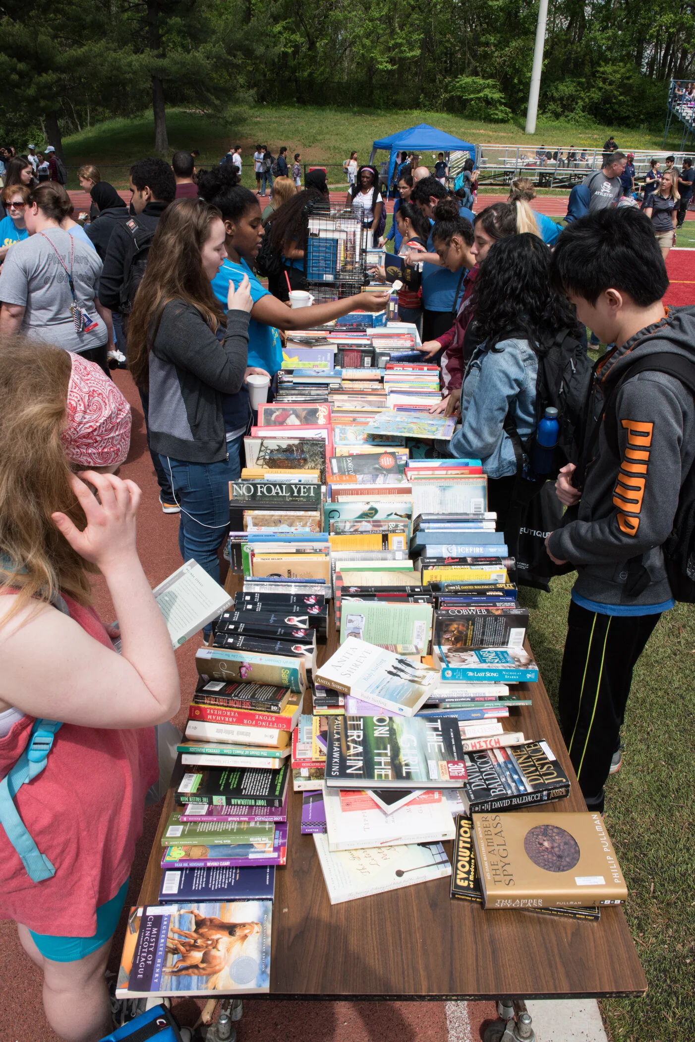 People shopping for books at an outdoor event on a running track.