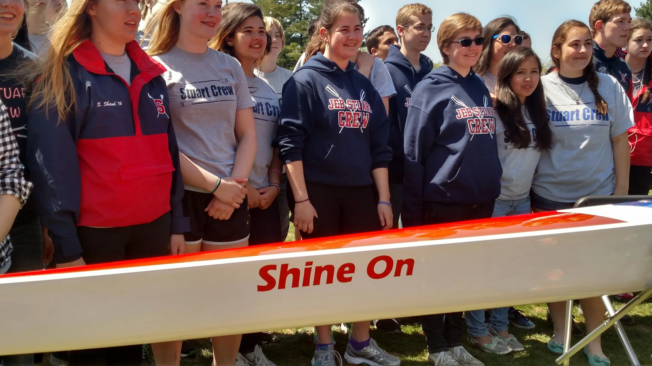 Group of young girls outdoors, standing behind a boat with the words 'Shine On' on it, smiling and wearing casual clothes.