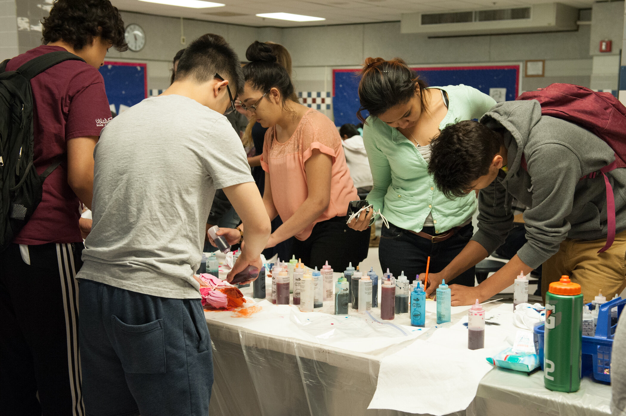 Group of young people around a table with bottles of dye, engaged in a tie-dye activity.