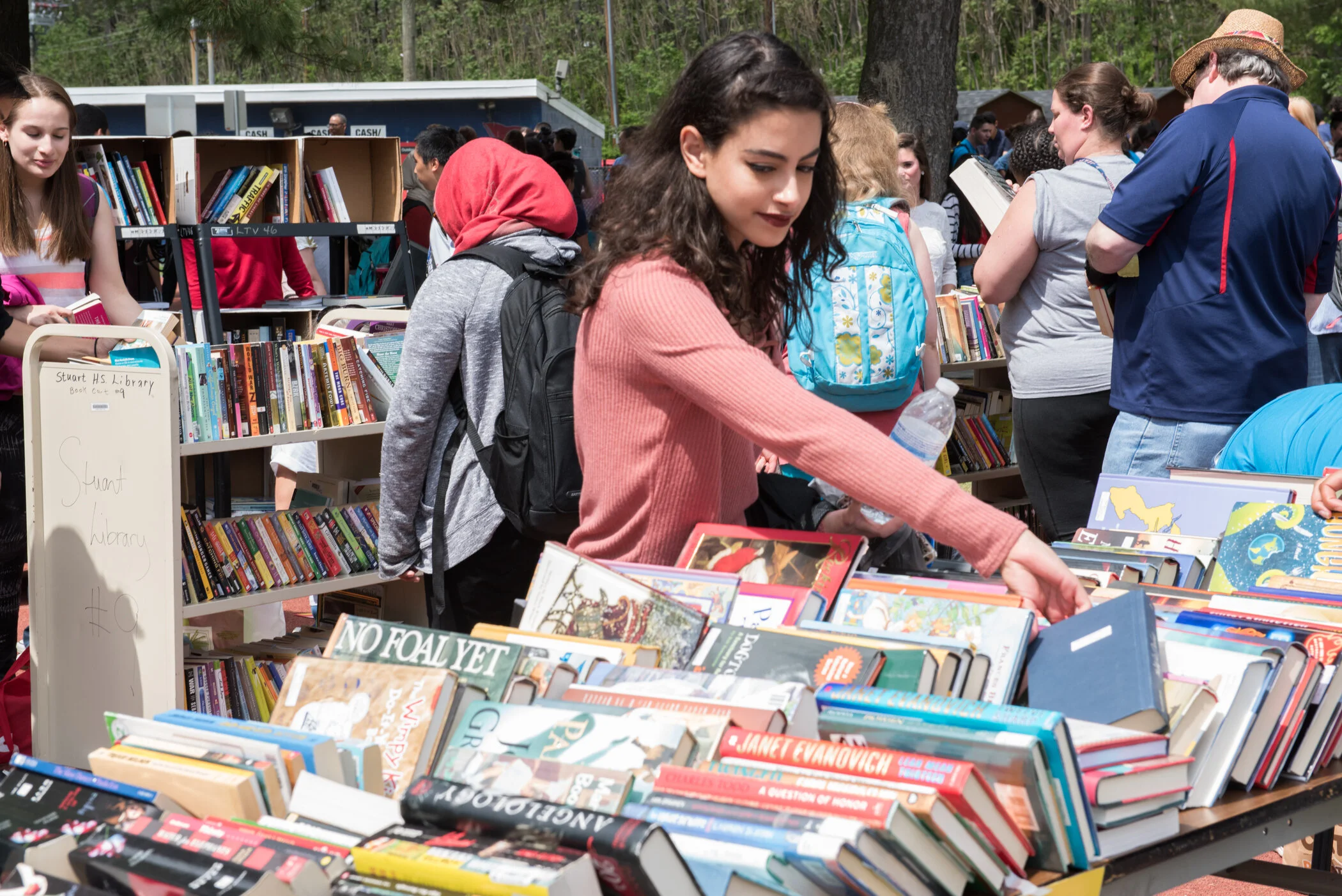People browsing books at an outdoor book sale or market, with tables filled with books and a crowded atmosphere.