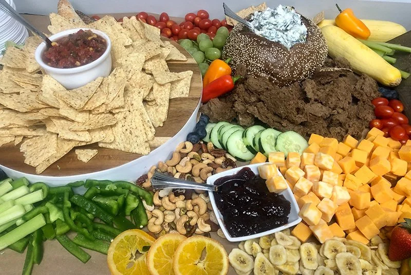 A large snack platter with vegetables, cheeses, fruit, chips, salsa, and dips.