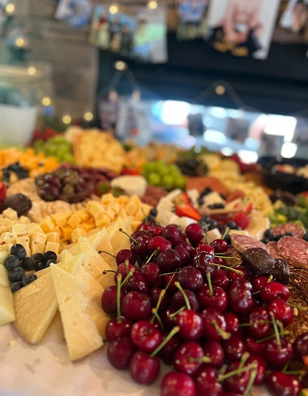 Close-up of a cheese and fruit platter with cherries, grapes, strawberries, and assorted cheeses on a wooden table.