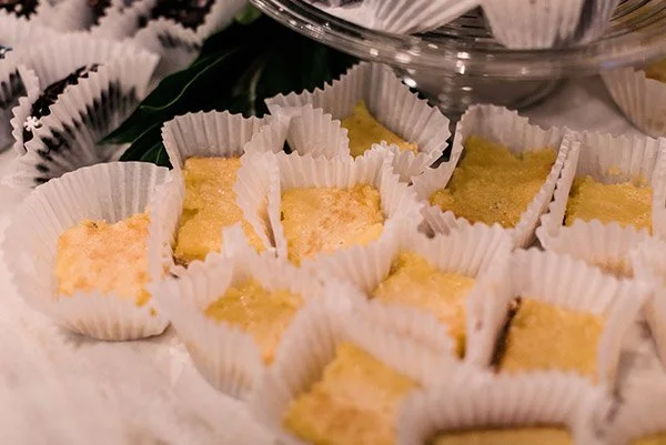 Small yellow cake bites in white paper cups on a tray.