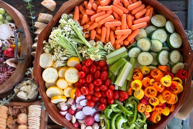 Colorful assortment of sliced vegetables including cherry tomatoes, cucumbers, carrots, radishes, celery, yellow squash, green bell peppers, orange and red bell peppers, and cauliflower