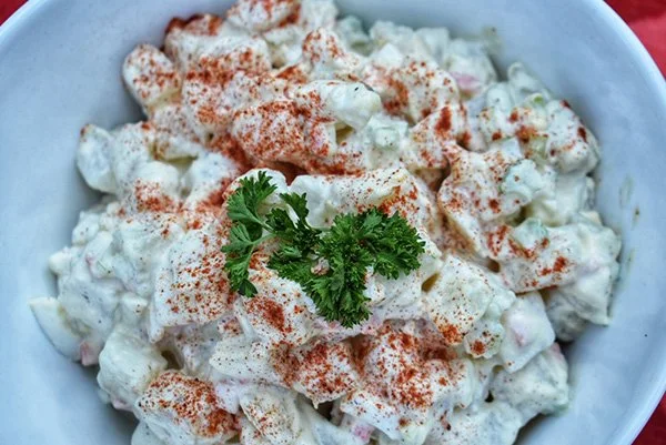 A bowl of potato salad topped with paprika and garnished with cilantro.