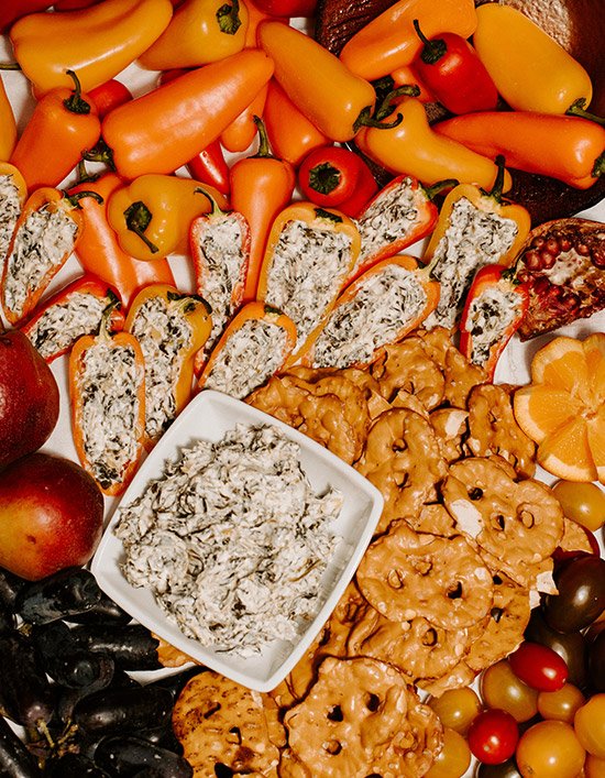 Assorted colorful peppers, apples, grapes, and cheese-filled bread slices with a bowl of creamy dip on a platter.