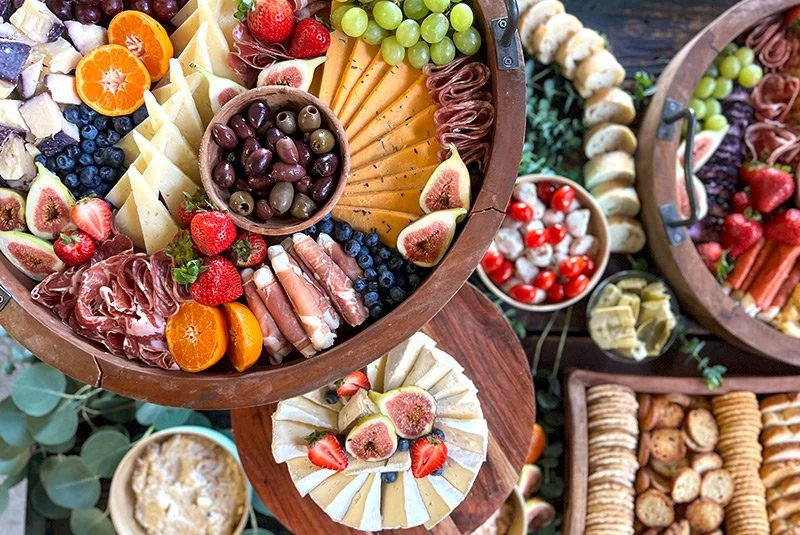 Assorted cheese, grapes, strawberries, figs, oranges, blueberries, olives, cured meats, and crackers on a charcuterie board.