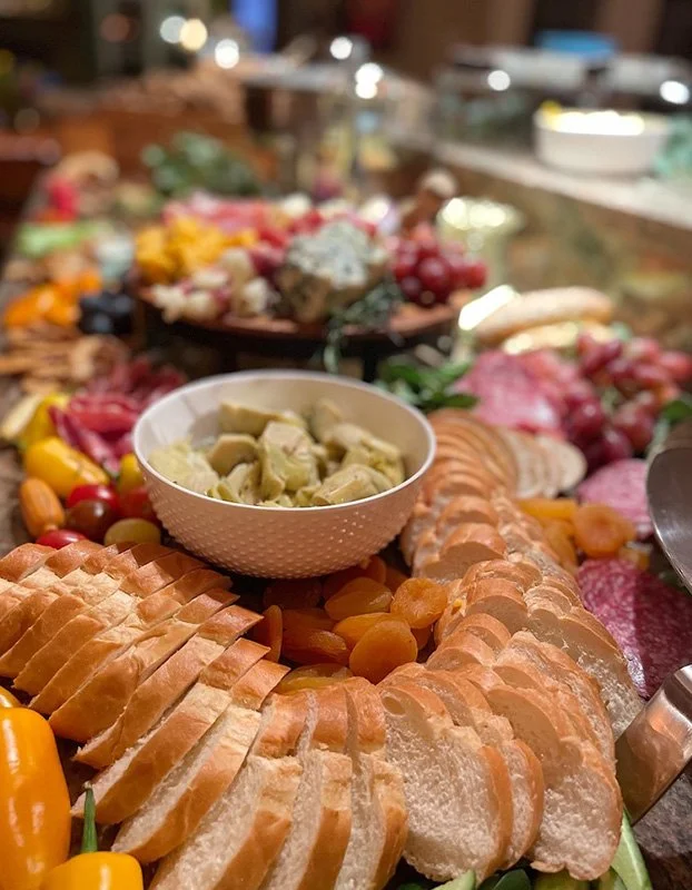An assortment of deli meats, cheeses, grapes, cherry tomatoes, and a bowl of artichoke dip on a buffet table.