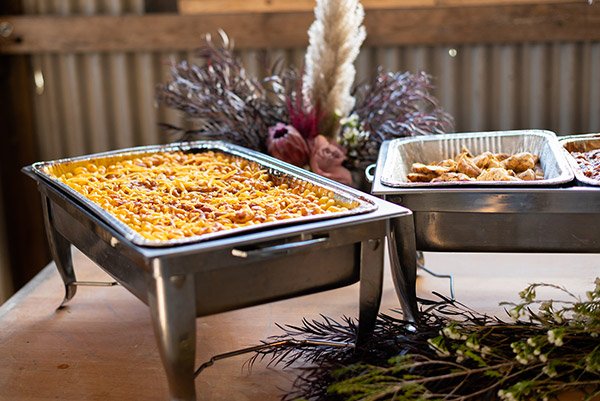 Food buffet with baked casserole and glazed chicken, decorated with flowers and dried plants.