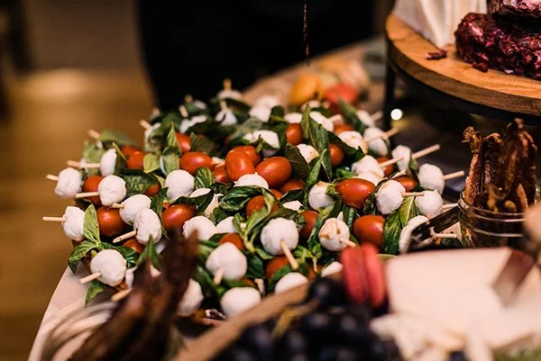 A platter of caprese bites with cherry tomatoes, mozzarella balls, and fresh basil leaves on skewers.