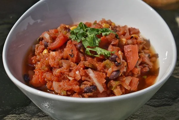 Bowl of chili with ground meat, beans, chopped tomatoes, and garnished with cilantro.