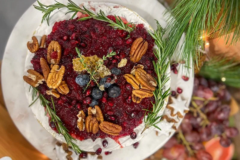 Holiday dessert topped with mixed berries, pecans, rosemary sprigs, and decorative leaves on a white plate.