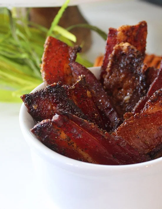 Close-up of crispy, cooked pork ribs in a white bowl with garnished greens in the background.