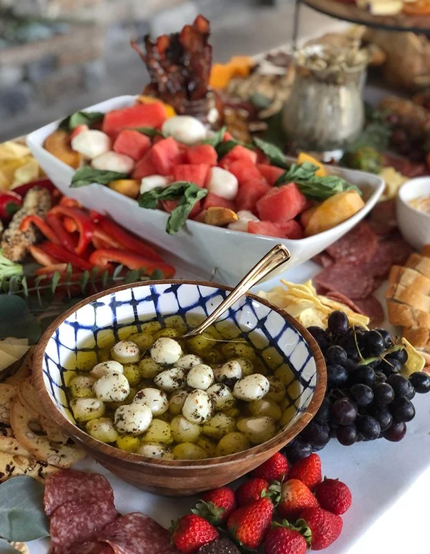 Close-up of a charcuterie and antipasto platter with fresh berries, mozzarella balls, watermelon, tomatoes, and various cured meats and cheeses.