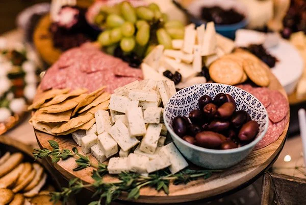 Cheese, crackers, grapes, olives, and assorted meats on a wooden platter for a charcuterie board.