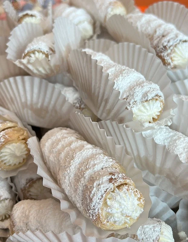 Cream-filled pastry rolls dusted with powdered sugar in white paper cups.