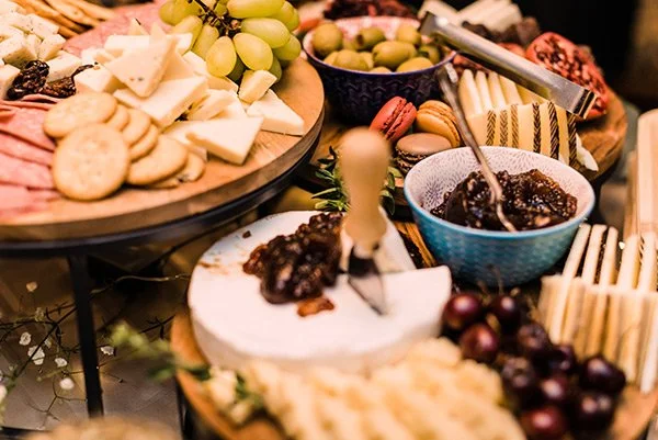 Cheese, green grapes, crackers, purple grapes, cookies, and jam on a buffet table at a party or gathering.