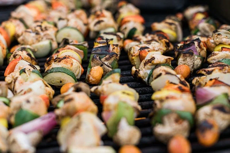 Skewers of grilled vegetables on a barbecue grill, including zucchini, yellow squash, and cherry tomatoes.