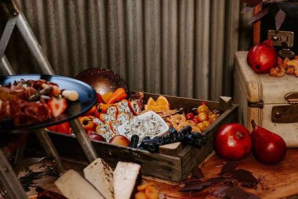 A rustic wooden table with a tray of assorted fresh fruits, including grapes, apples, and berries, along with a small vintage suitcase and some fall leaves.