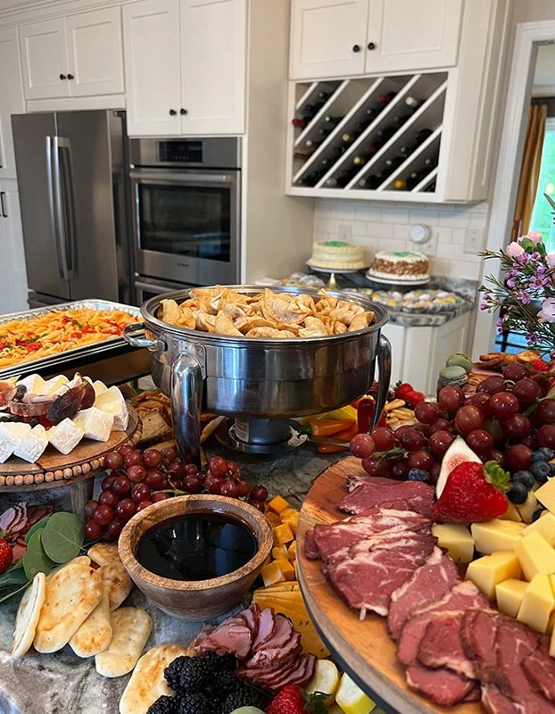 A feast with cheese, grapes, meats, and appetizers on a kitchen counter, with a white kitchen in the background.