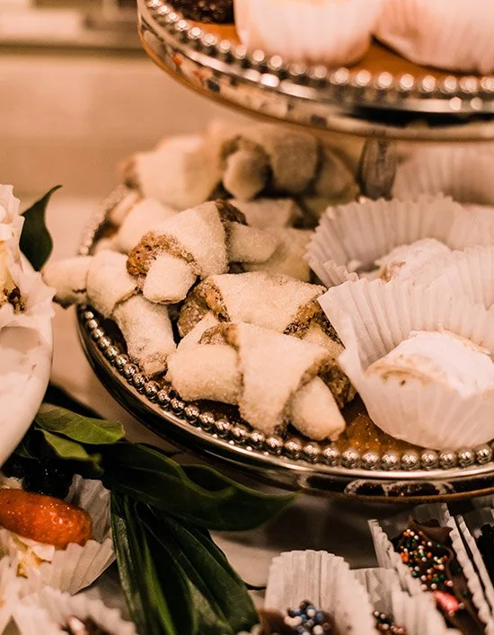 A silver tiered serving tray filled with powdered sugar-coated cookies and cupcakes in white paper cups.