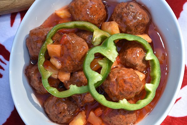 A bowl of meatballs in tomato sauce with sliced green bell peppers and chopped tomatoes.