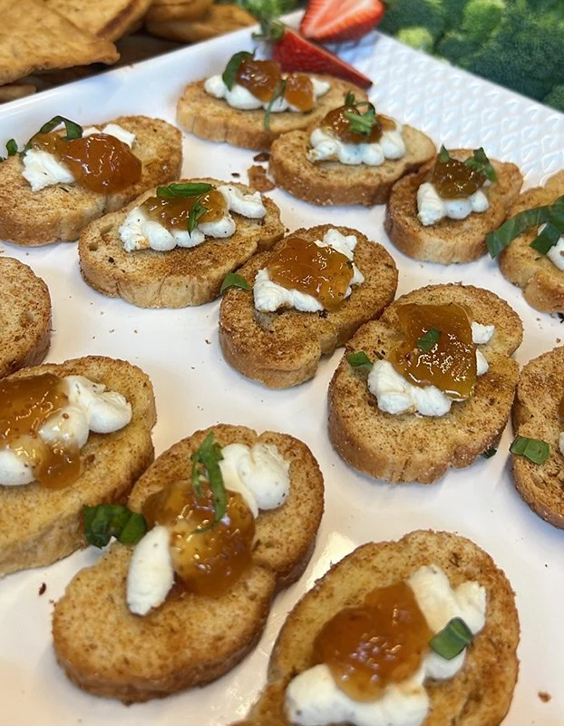 Crispy toasted bread slices topped with whipped cream, orange marmalade, and green onion, served as appetizers on a white platter.