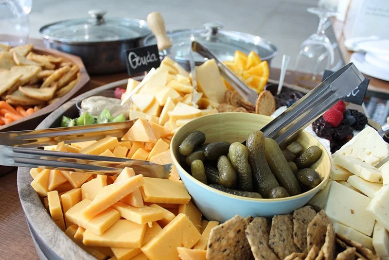 Assorted cheeses, pickles, crackers, and berries on a cheese platter at a gathering.