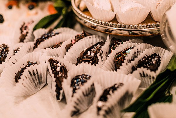 Assorted chocolate pretzels decorated with colorful sprinkles on a white tray with white paper cups.