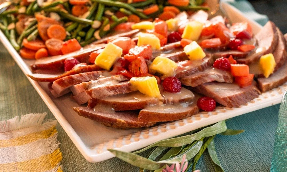 Sliced roast beef topped with pineapple chunks, cranberries, and diced carrots, served on a platter with cooked green beans and sliced carrots on the side.