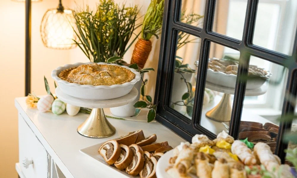 Easter dessert table with pie on a white pedestal, decorated cookies, spring-themed candies, and a mirror reflecting additional desserts in a cozy, decorated room.