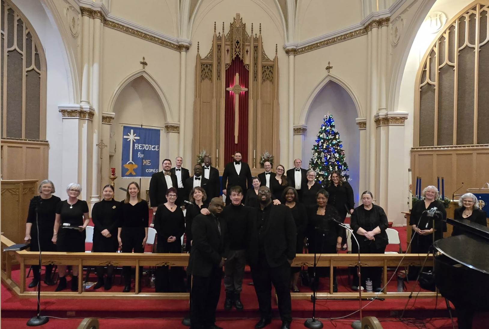 Members of the Tutti Voce Collective community choir standing together after a concert inside a church sanctuary, dressed in black performance attire.