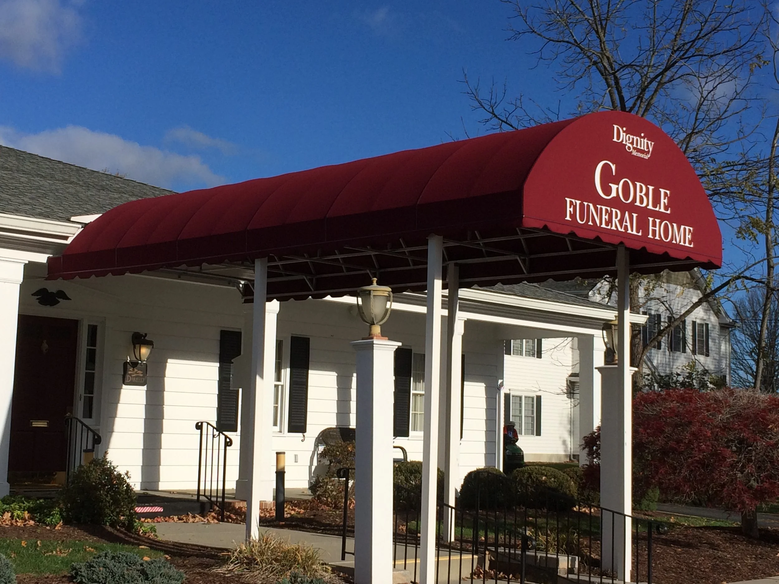 Goble Funeral Home with red canopy and white building in the background, on a sunny day.