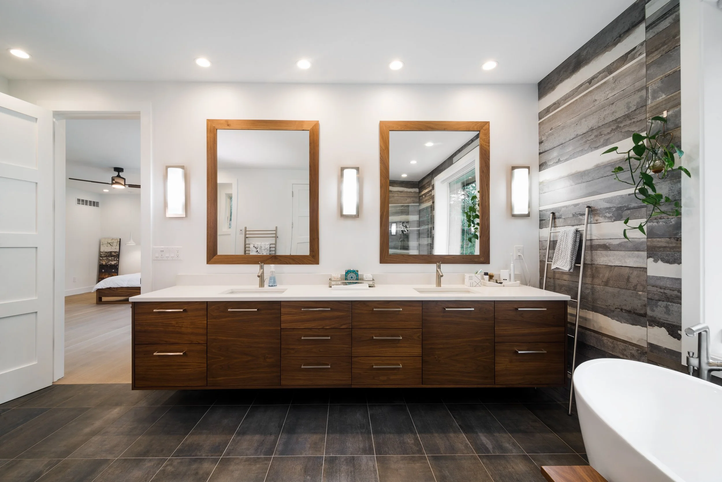 Modern bathroom with double vanity, large mirrors, wood accents, white countertop, and a freestanding bathtub, with a rustic wood plank accent wall.