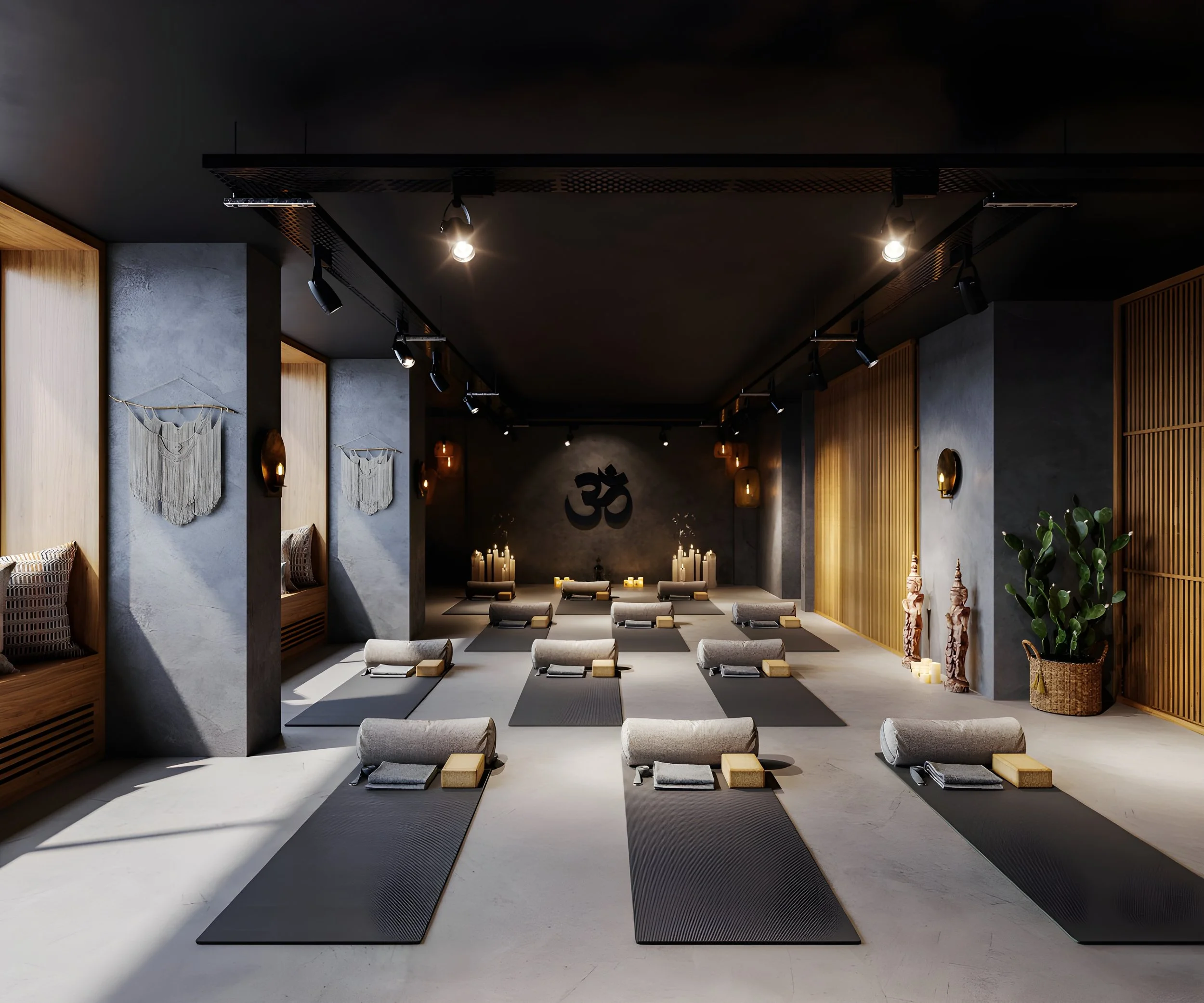 A serene yoga studio with black mats, bolsters, candles, and decor, featuring a large Om symbol on the wall.