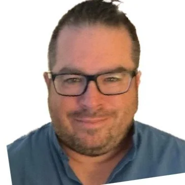 Close-up of a man with glasses, short hair, and a slight smile, wearing a blue shirt.