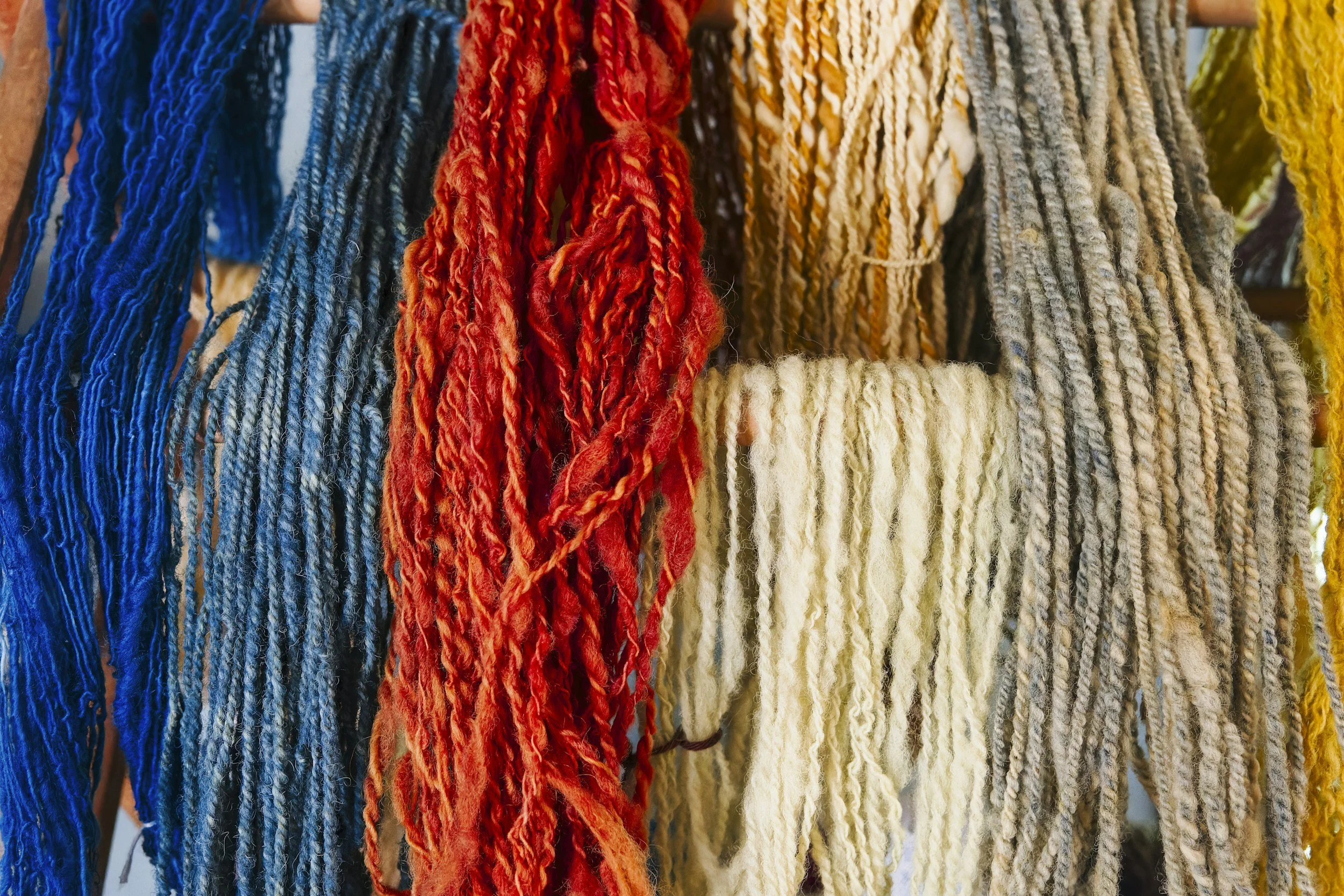 Colorful yarn skeins hanging, including red, blue, gray, and cream.
