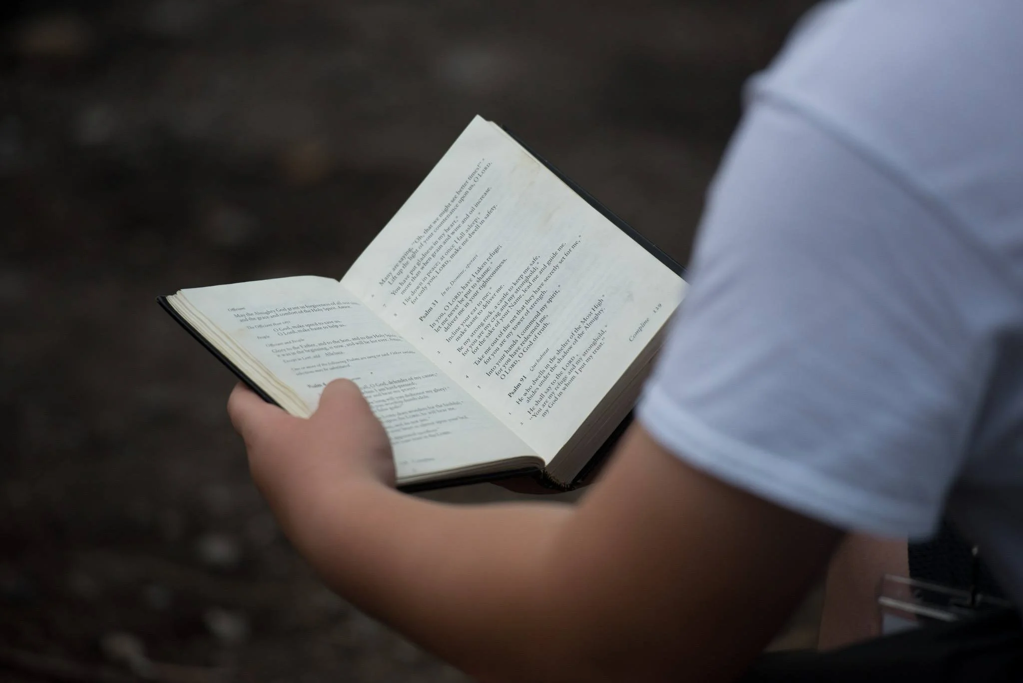 A person wearing a white shirt reading a Bible outdoors.