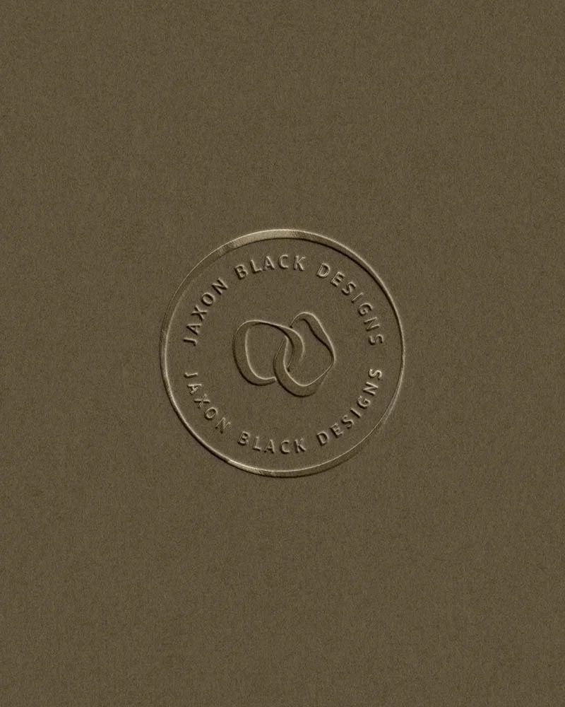 Embossed logo on a surface with the Jaxon Black Designs surrounding a stylized design in the center
