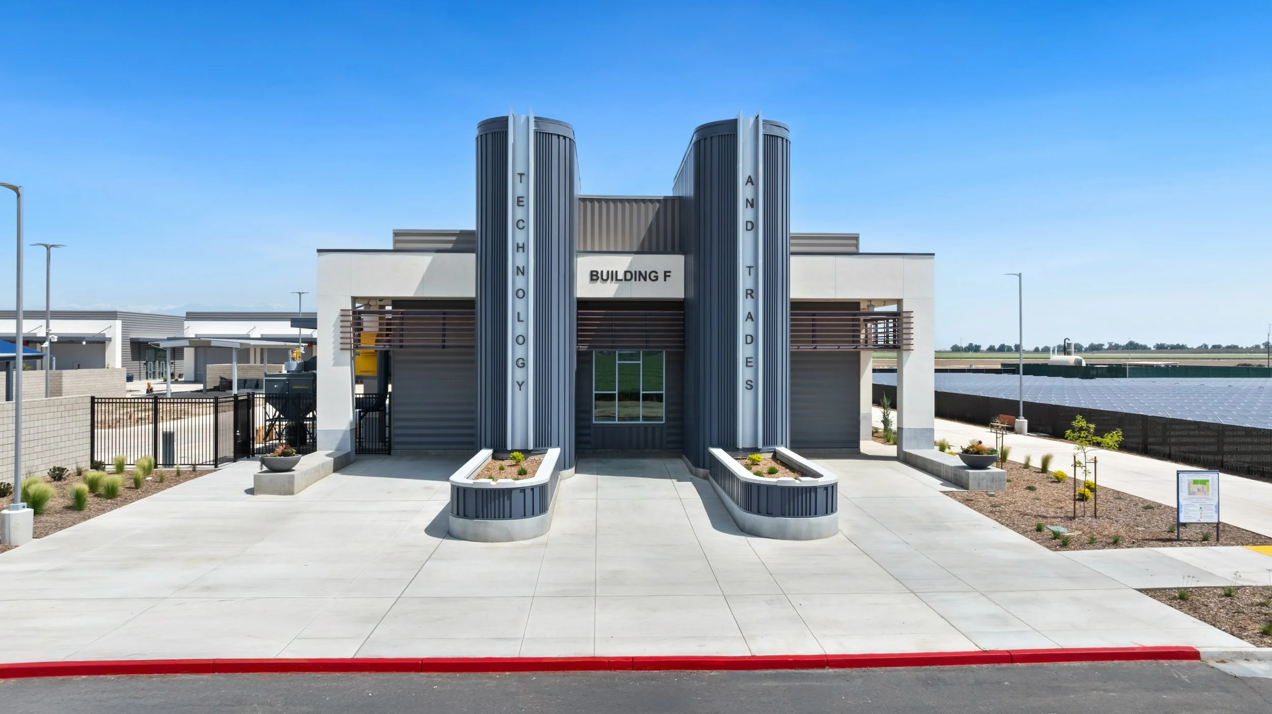 Front of a modern building labeled 'Building F' with vertical signposts reading 'Technology' and 'And Trades'.