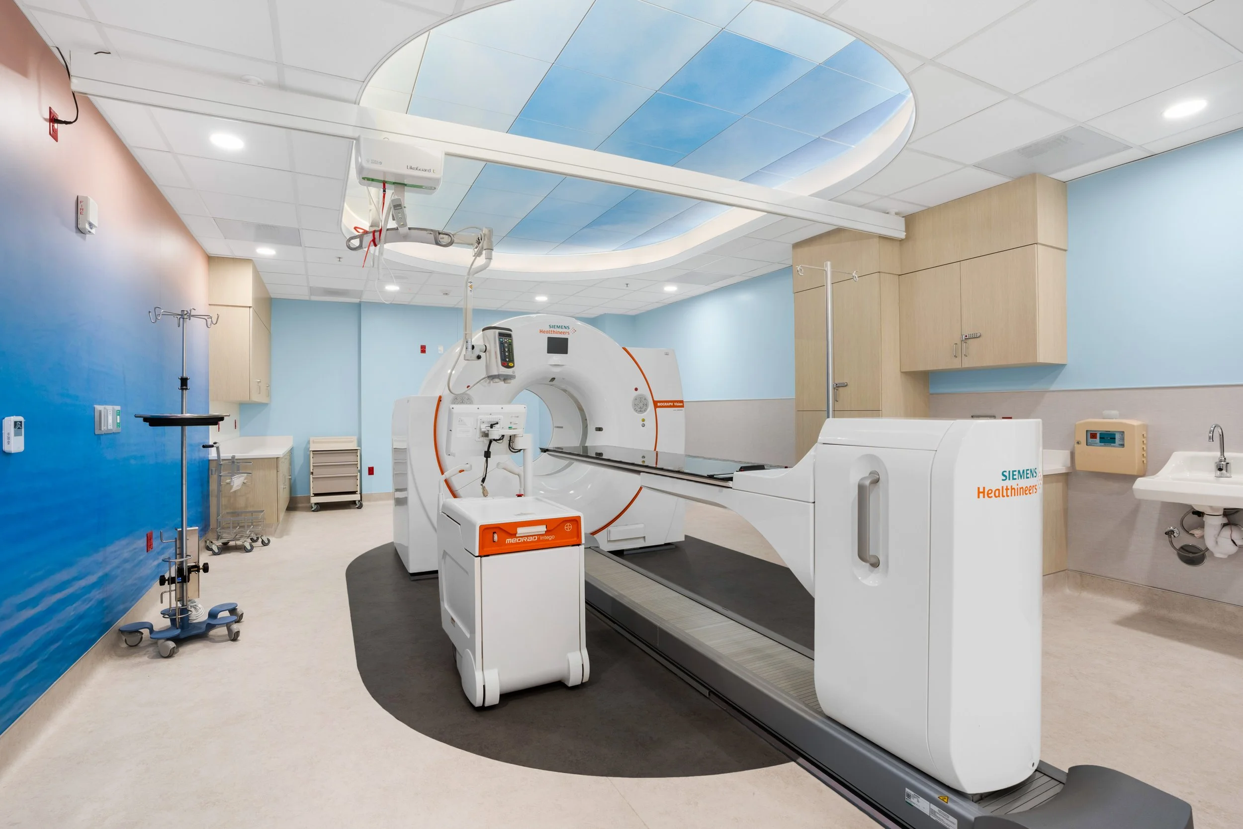 A modern medical imaging room with a  scanner, hospital equipment, and ceiling designed to resemble a blue sky with clouds.