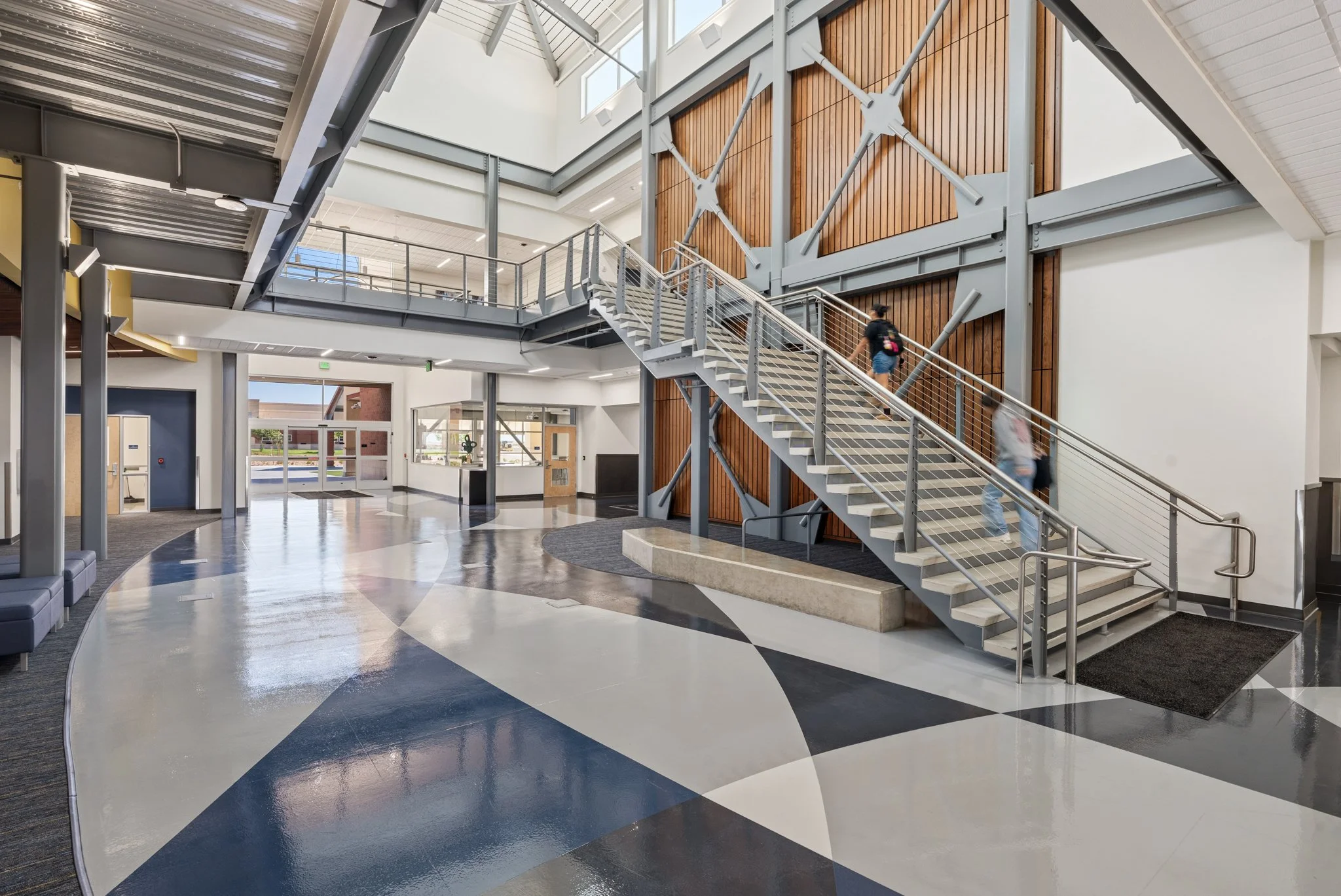 Interior of a modern building with a staircase, large windows, and a polished floor with geometric patterns.