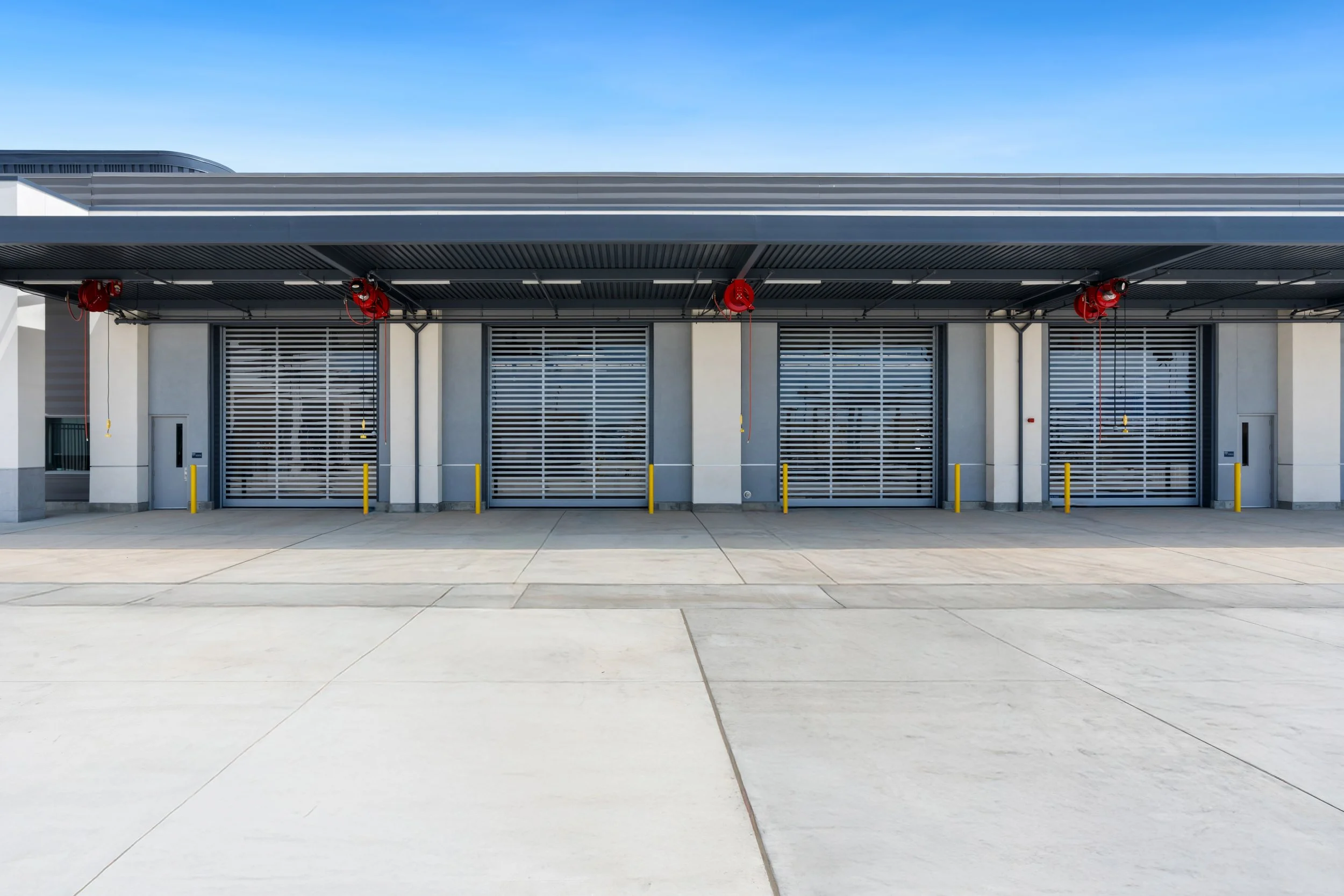 An exterior view of a modern building with large ventilation grilles and red fire alarm equipment under a gray canopy, with a clear blue sky