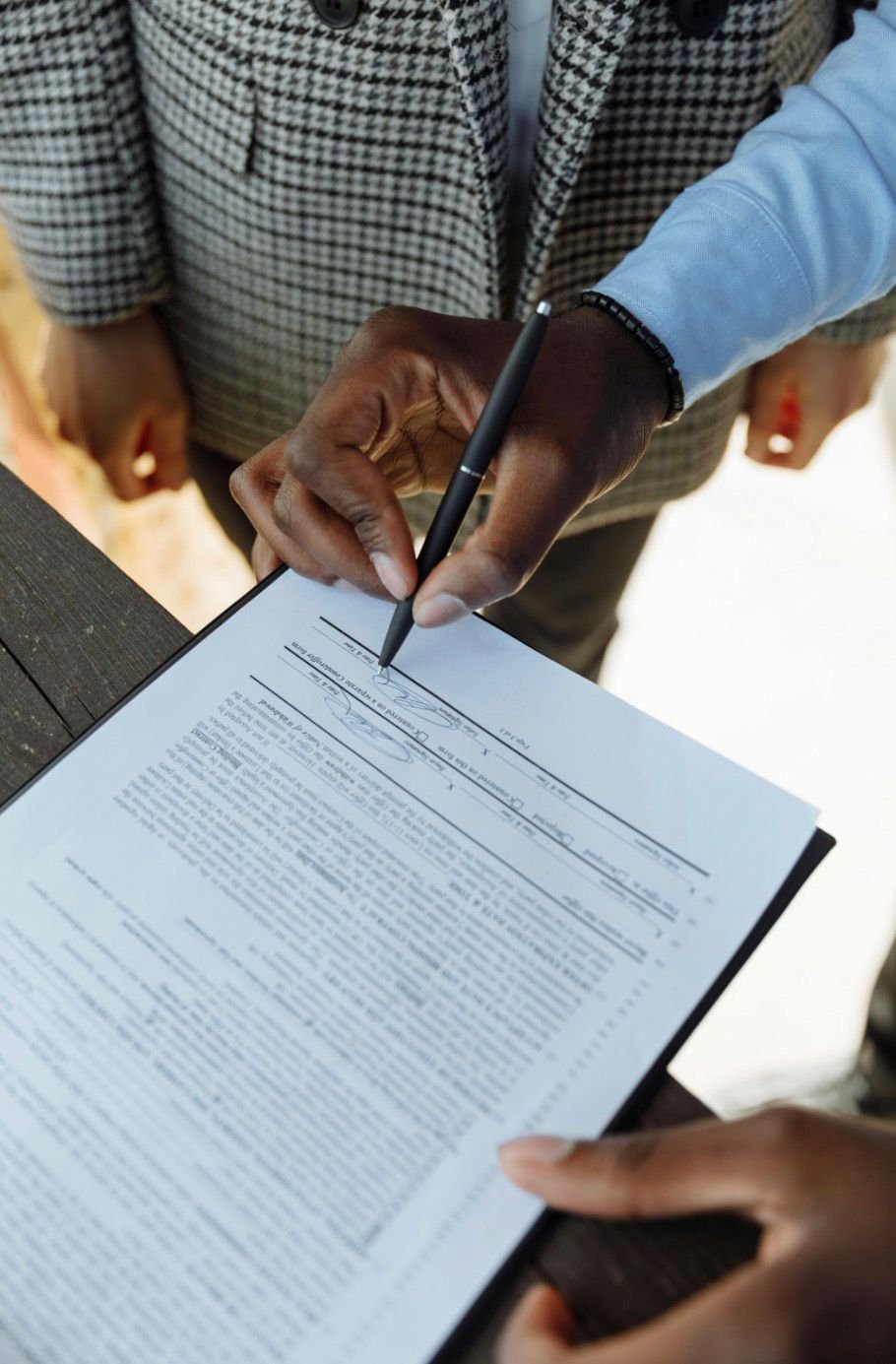 Person signing a legal document with a pen, viewed from above.