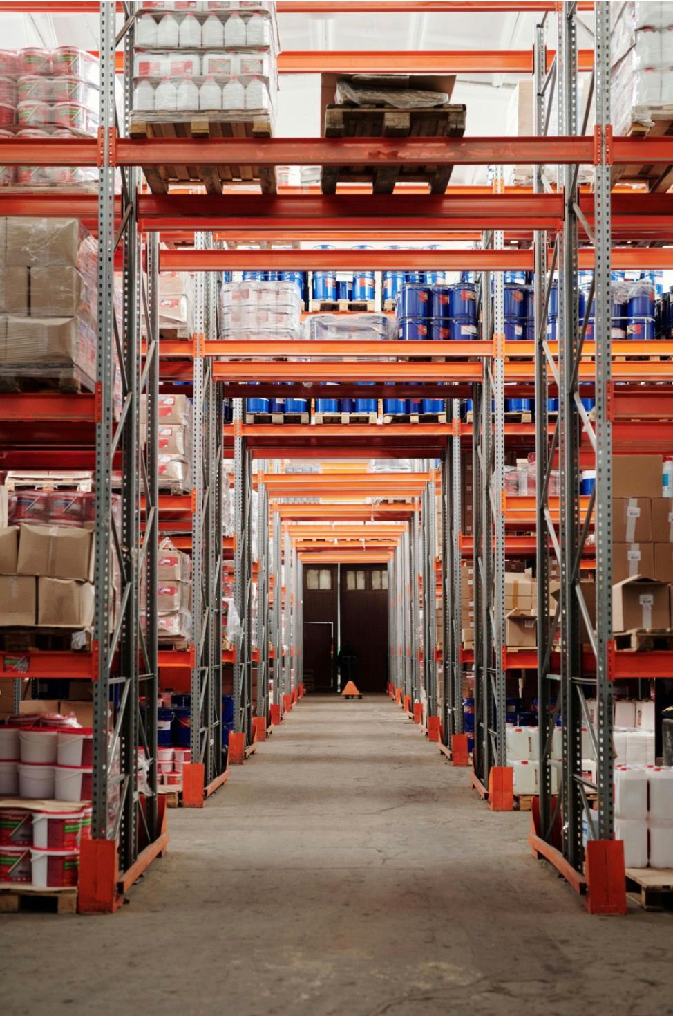 Long aisle in a warehouse with high shelf racks filled with boxes, buckets, and packages.