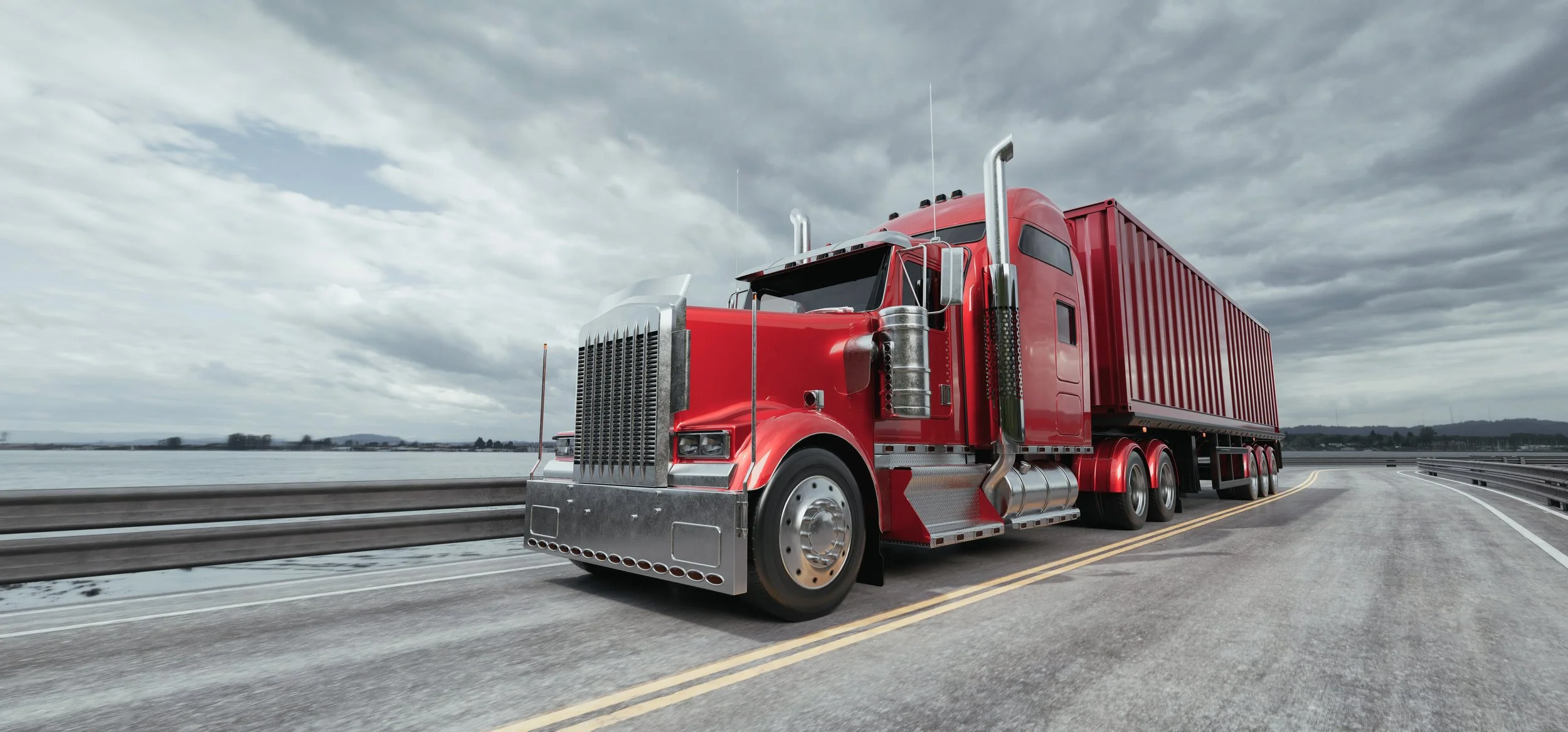 A large red semi-truck driving on a bridge over water under a cloudy sky.
